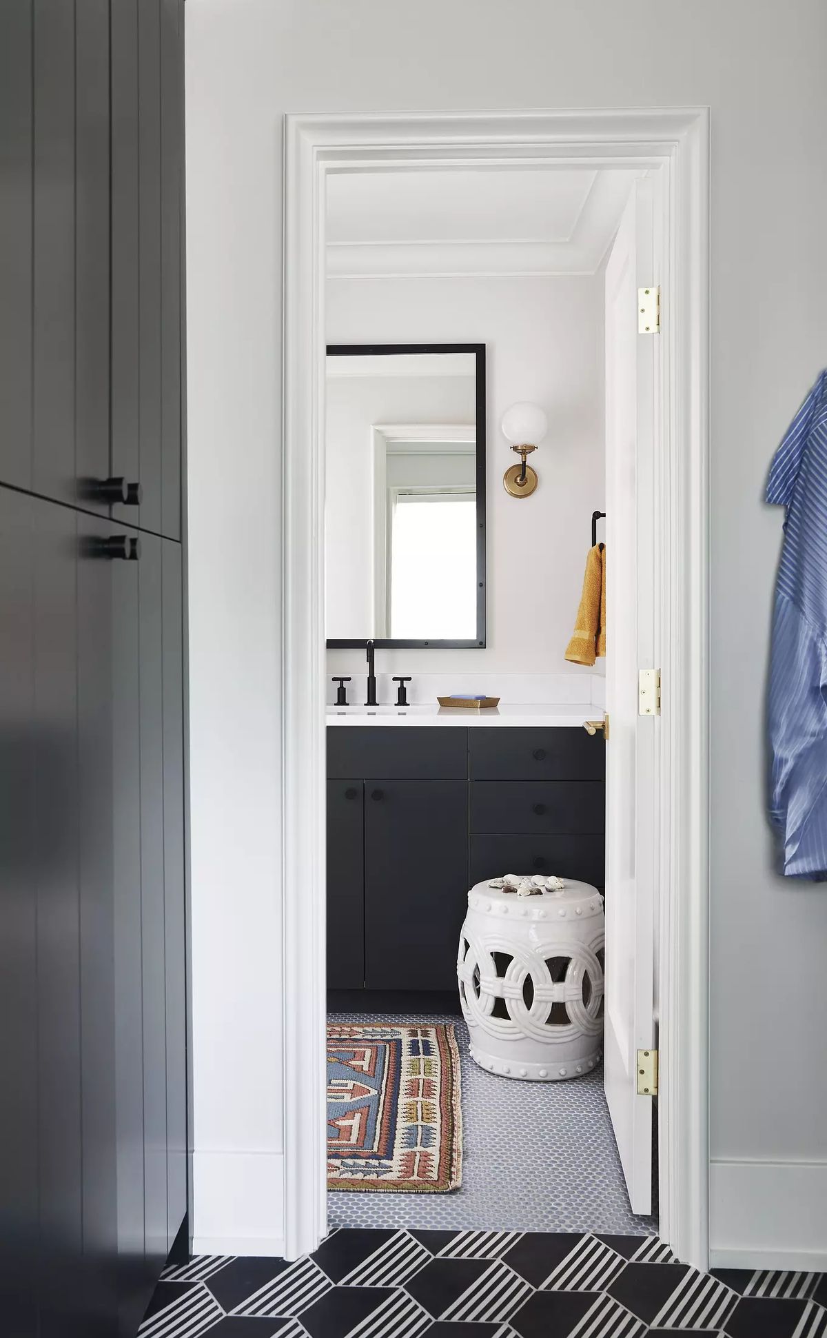 Bathroom with black cabinetry, mirror, wall-mounted faucet, patterned floor, stool, and colorful rug