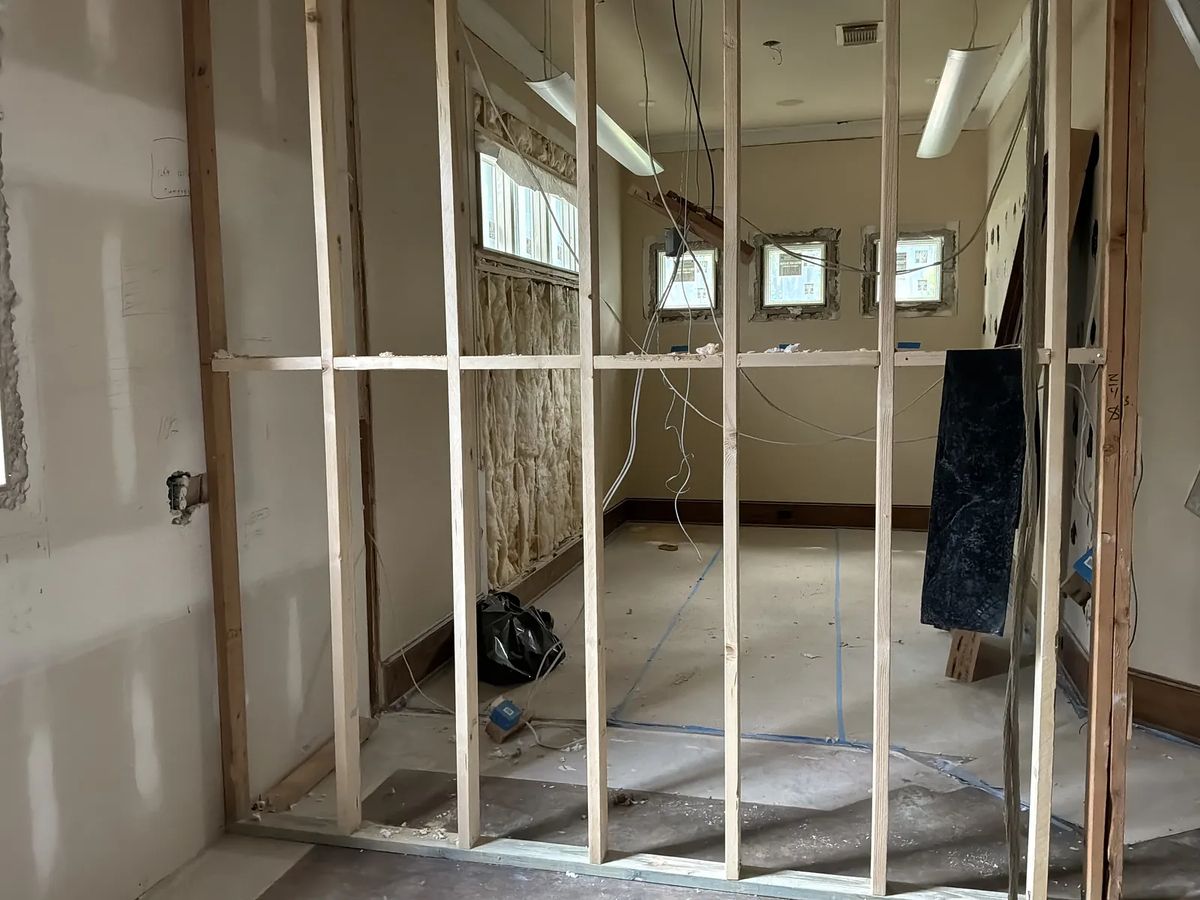 Unfinished room with exposed framing, electrical wiring, bare walls, and two small windows.