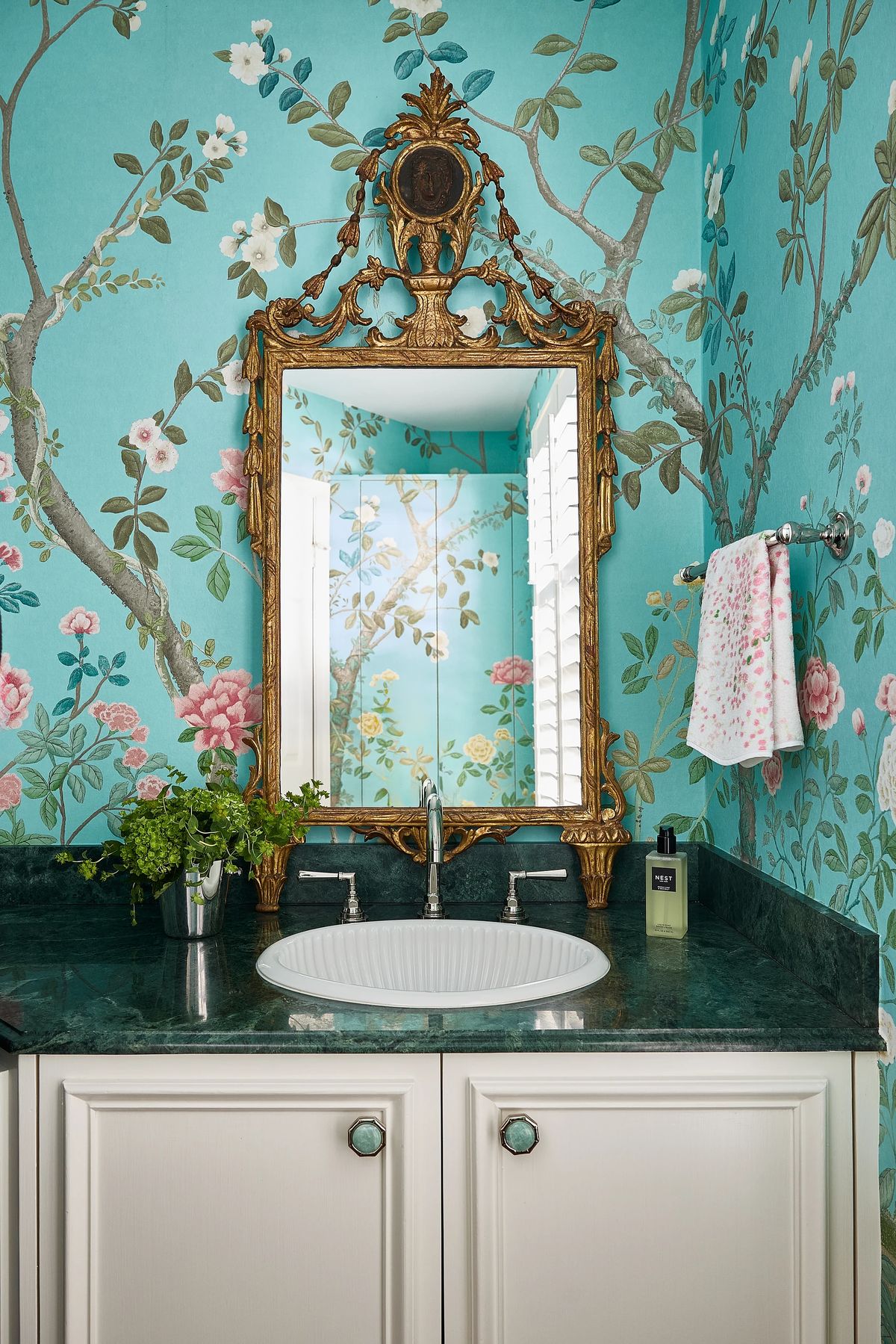 Bathroom with curved sink, green marble countertop, floral wallpaper, and ornate gold mirror.