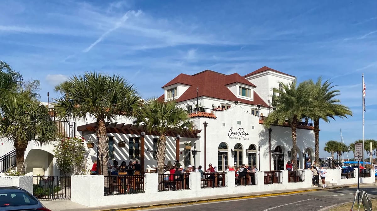 Exterior view of a two-story building with red-tiled roof, palm trees, and outdoor seating area.