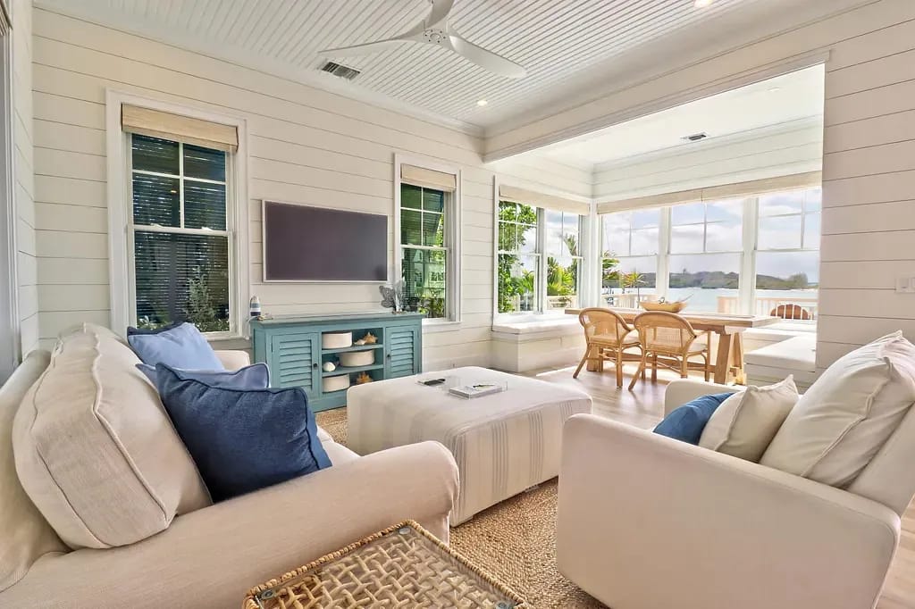 Living room with white sofas, blue cushions, beige rug, blue console, and large windows offering outdoor views.