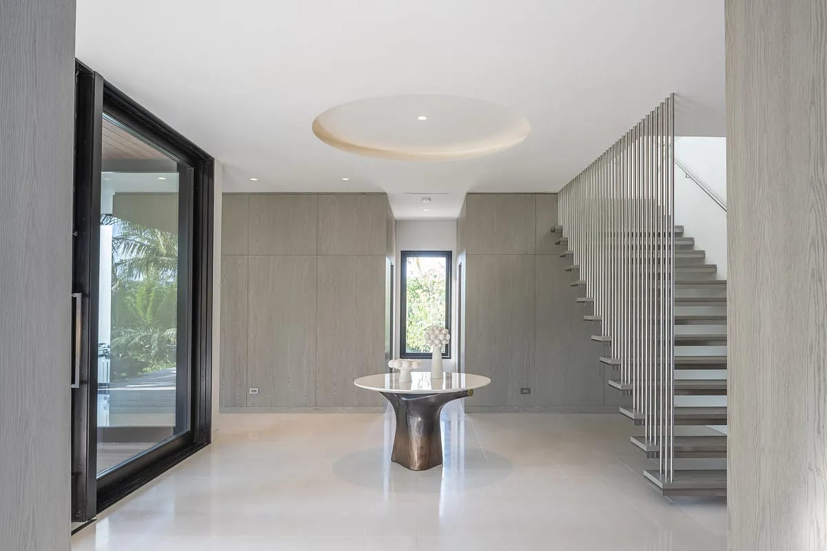 Foyer with round table, stair railing, large windows, light paneling, and circular ceiling detail