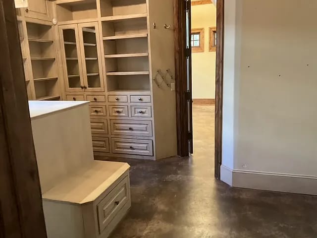 Closet with built-in shelves, drawers, and a seating area on polished concrete floor.
