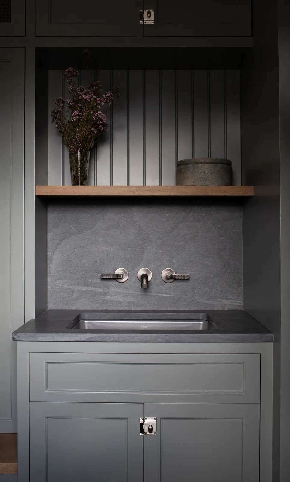 Laundry room with gray sink, countertop, cabinetry, wooden shelf, and decorative vase