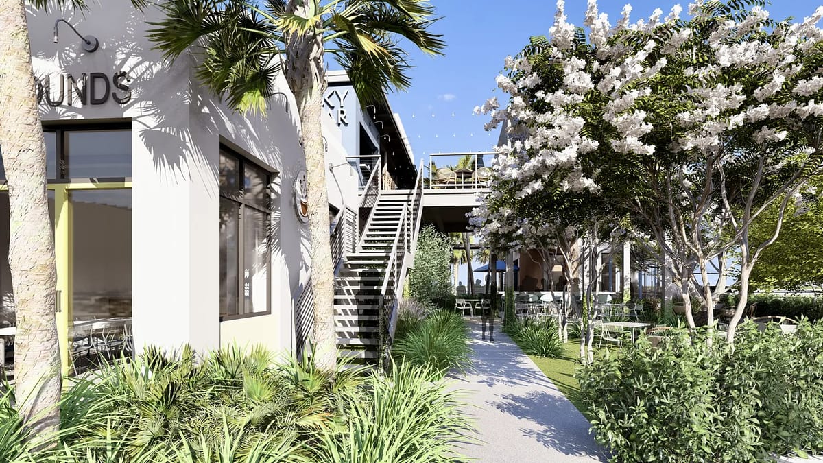 Exterior view with pathway, palm trees, flowering bushes, and a building with outdoor seating.