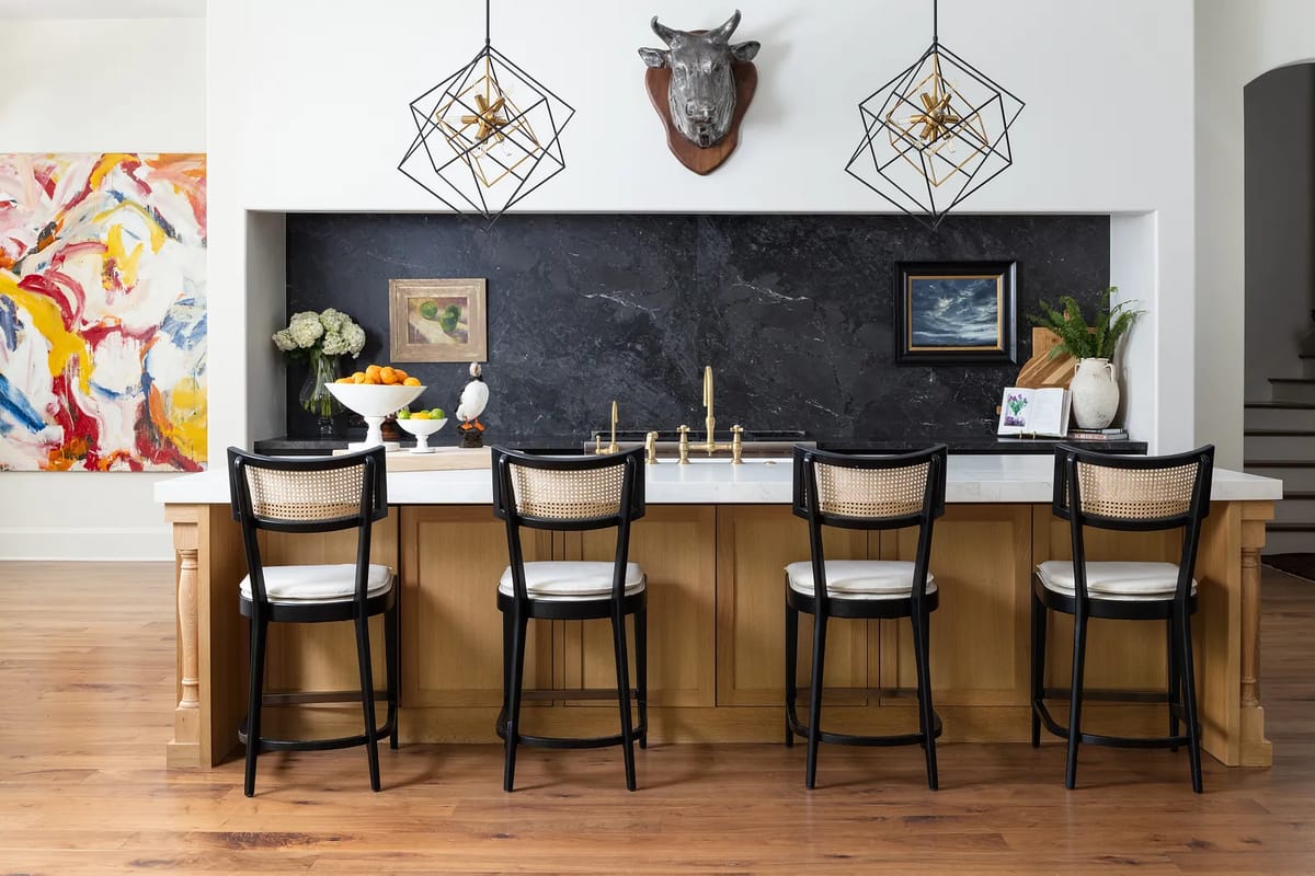 Kitchen with island, bar stools, marble countertop, dark stone backsplash, and decorative wall art.