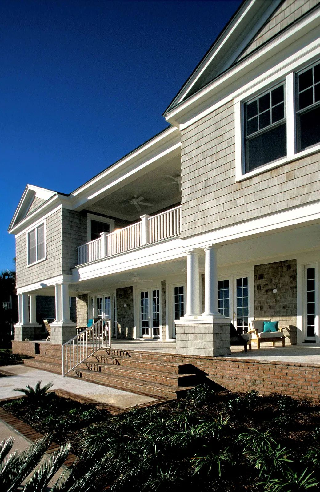 Exterior front view of a house with wooden siding, stone accents, columns, porch seating, and landscaping.