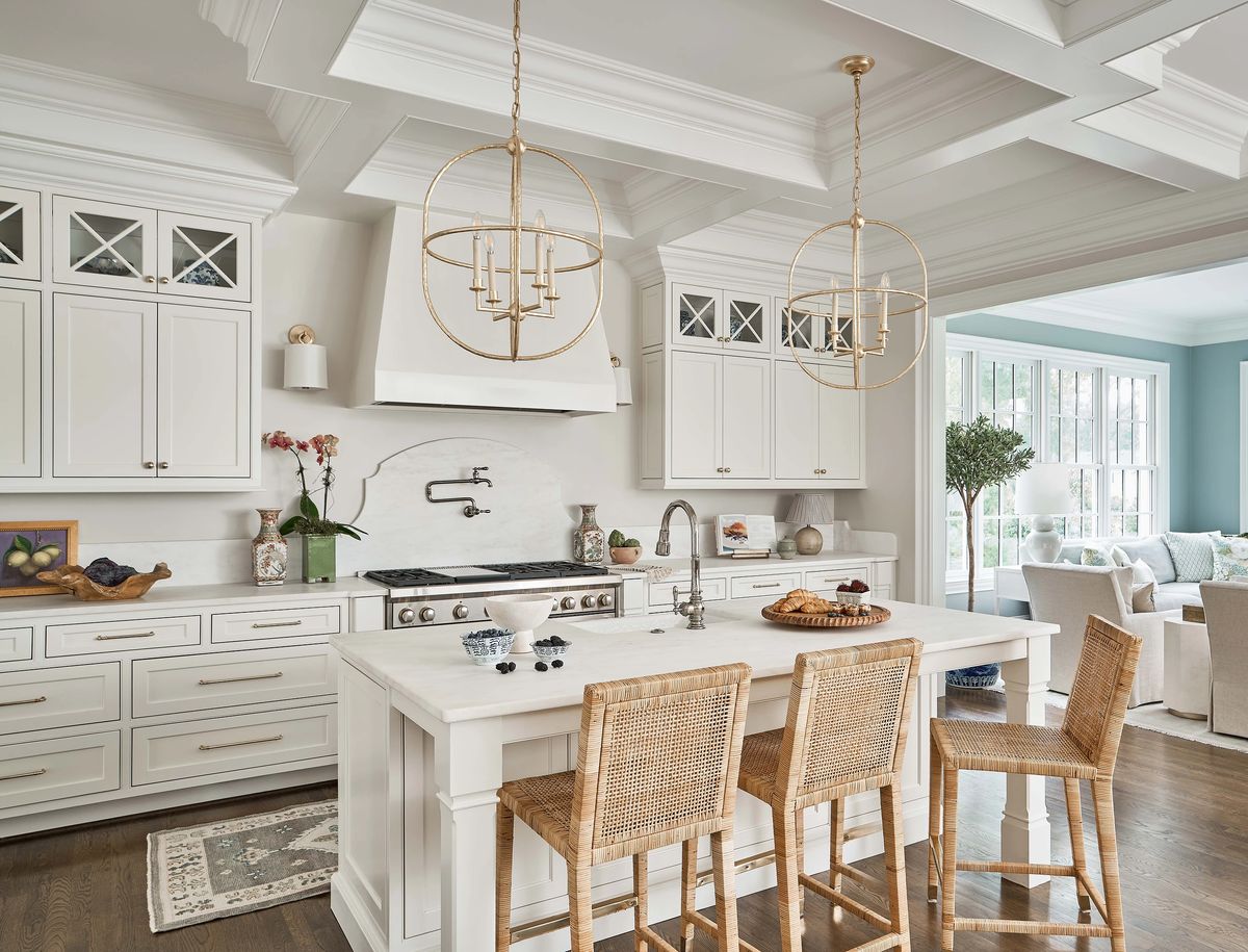 Kitchen with white cabinets, marble island, woven bar stools, and stainless steel appliances with decorative beams.
