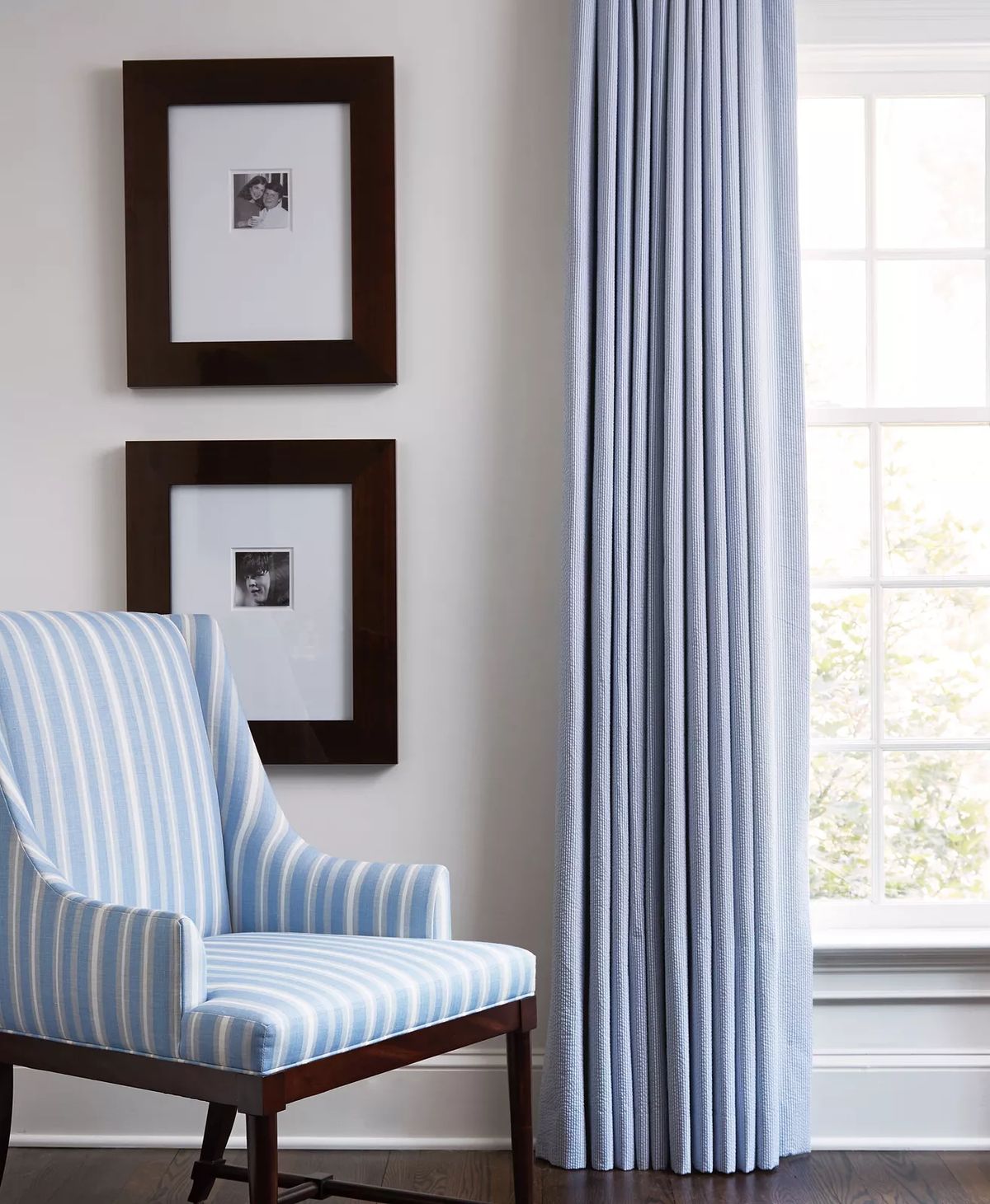 Seating area with striped blue chair, blue curtains, and framed pictures above the chair.
