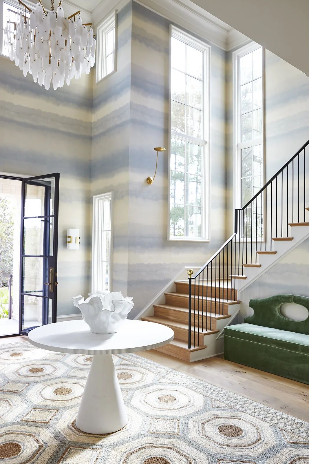 Foyer with round white table, green sofa, area rug, large windows, and staircase with black railing