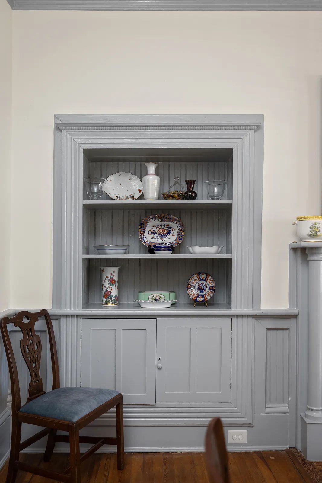 Dining room with built-in cabinet, decorative plates, vases, and wooden chair on wood flooring.