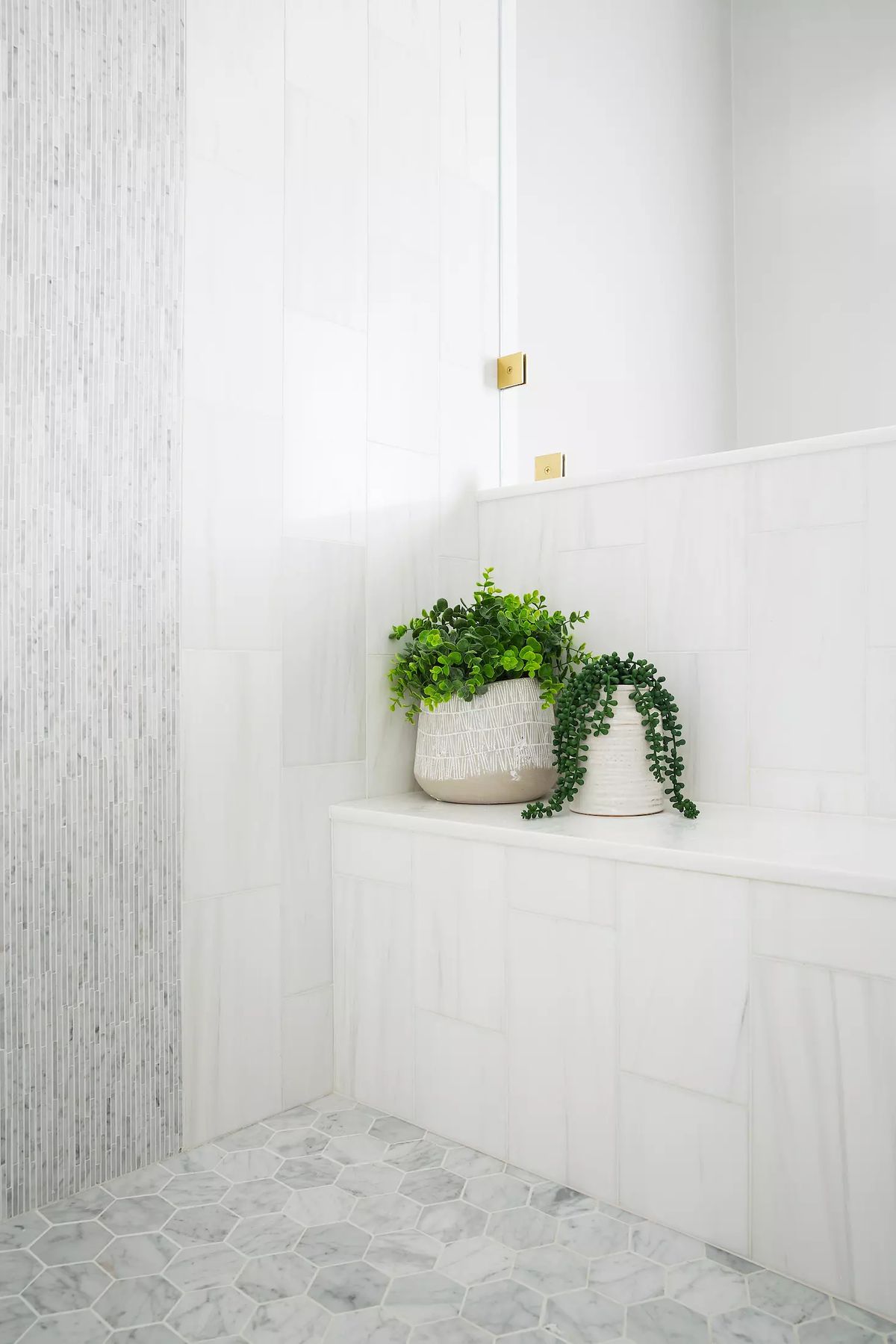 Bathroom with white marble walls, hexagon tile floor, built-in bench, and greenery in woven baskets