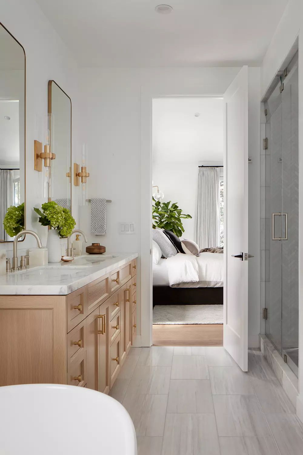 Bathroom with double vanity, marble countertop, mirrors, glass shower, and plants.
