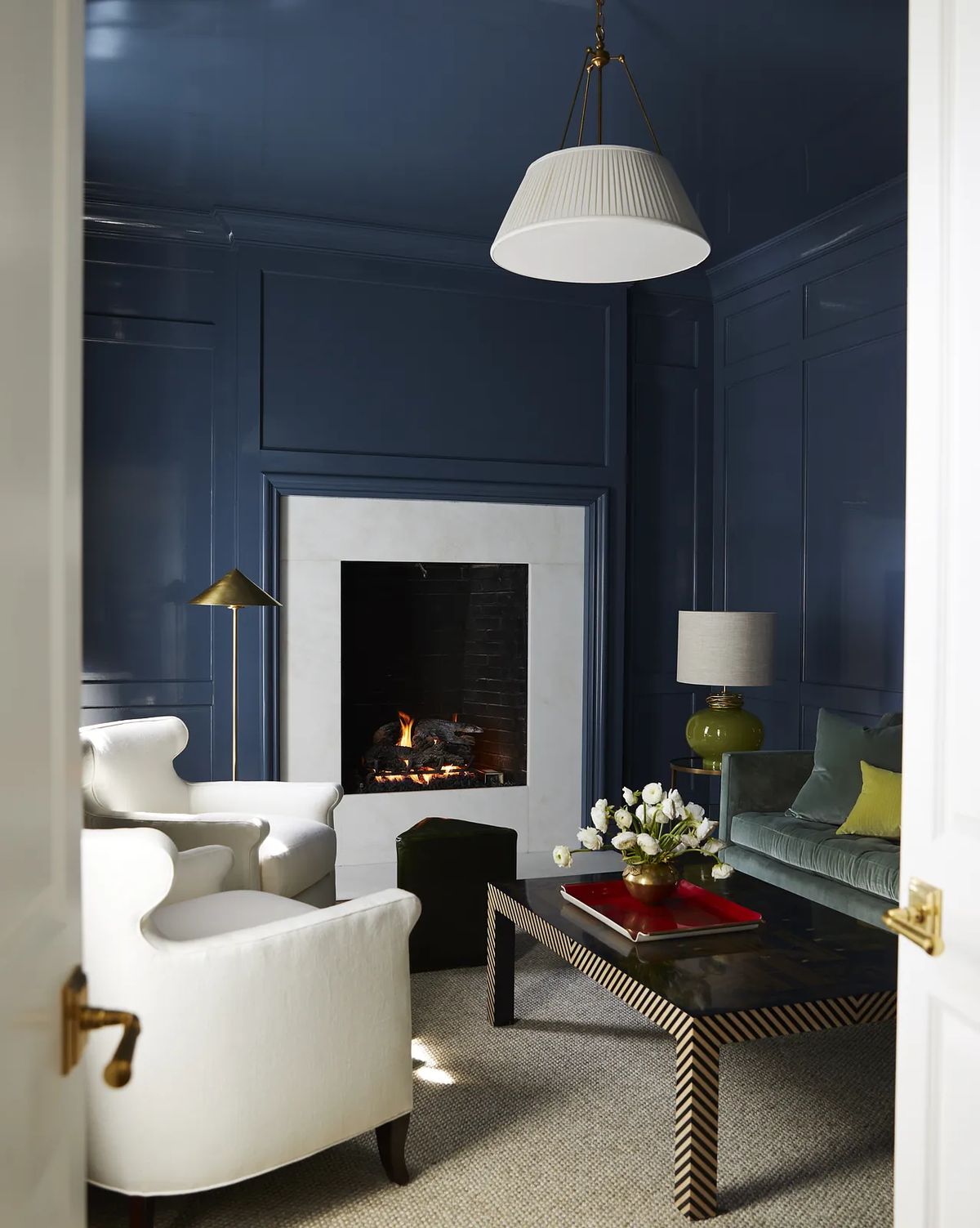 Living room with white armchairs, green velvet sofa, dark wood coffee table, and blue paneled walls with fireplace.