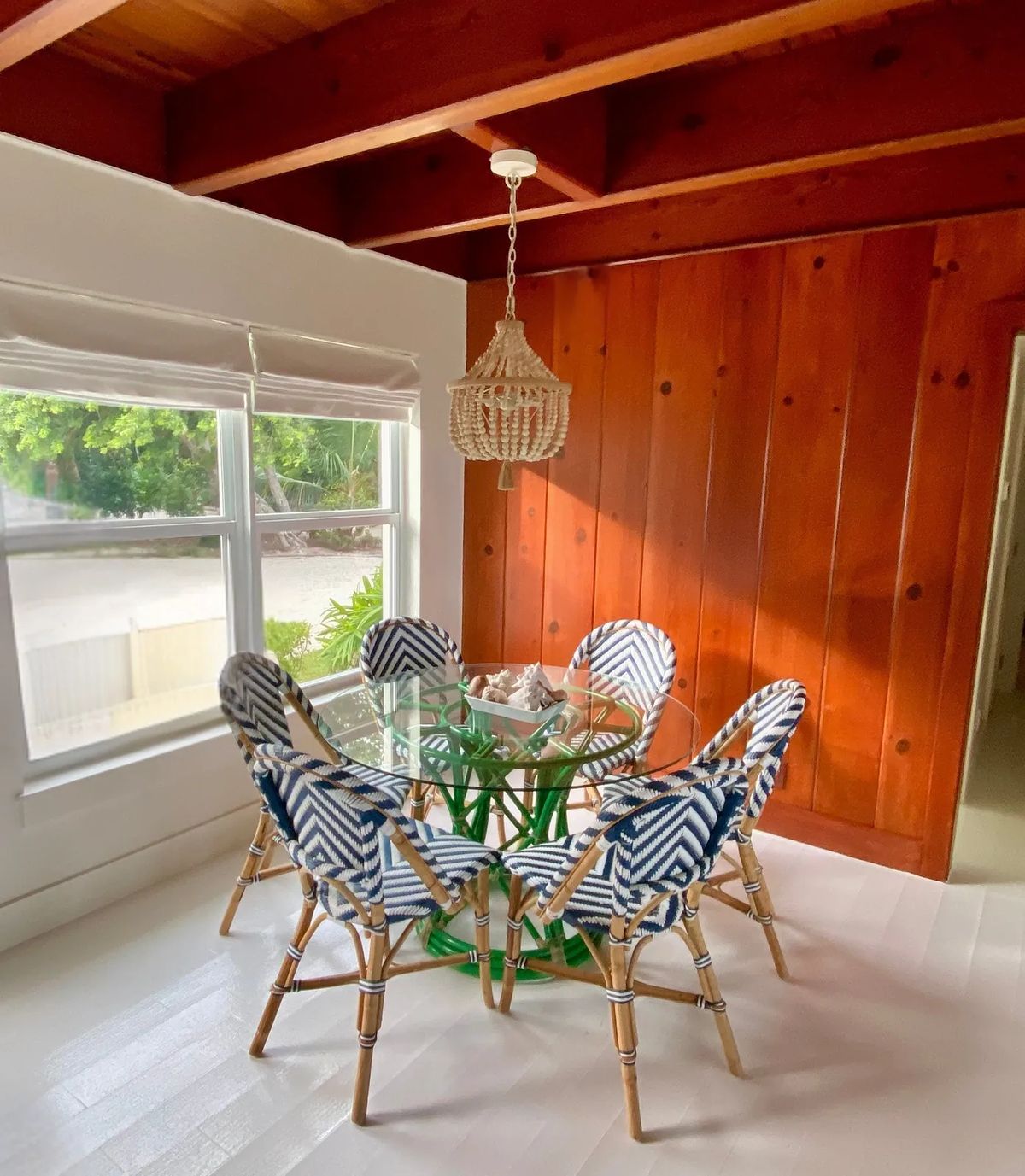 Dining room with round glass table, rattan chairs, wood-paneled walls, and woven pendant light