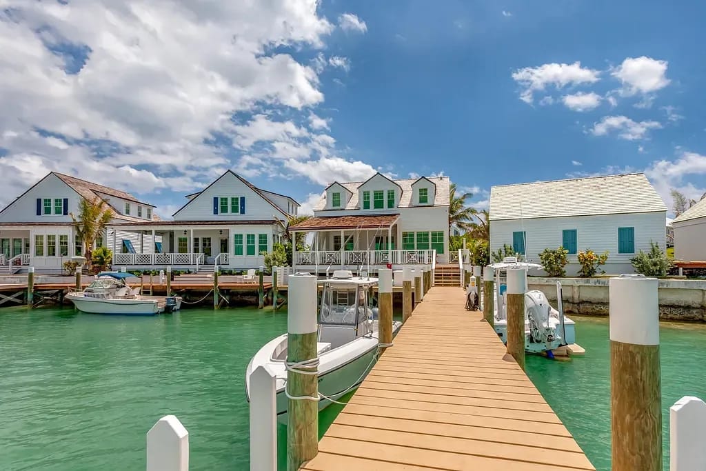 Waterfront scene with houses, wooden dock, and boats against a clear sky.