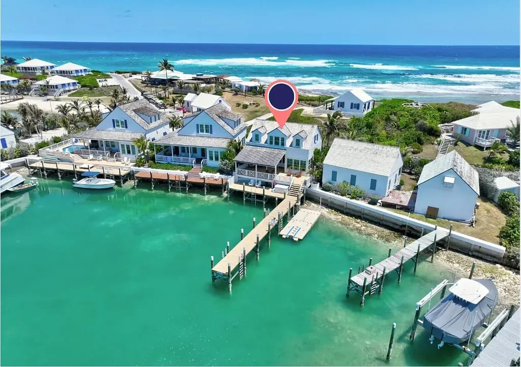 Aerial view of coastal homes, docks, and turquoise water with vegetation and clear skies.
