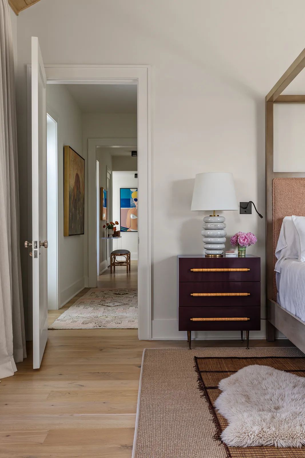 Bedroom with four-poster bed, nightstand, lamp, painting, and adjoining room door.