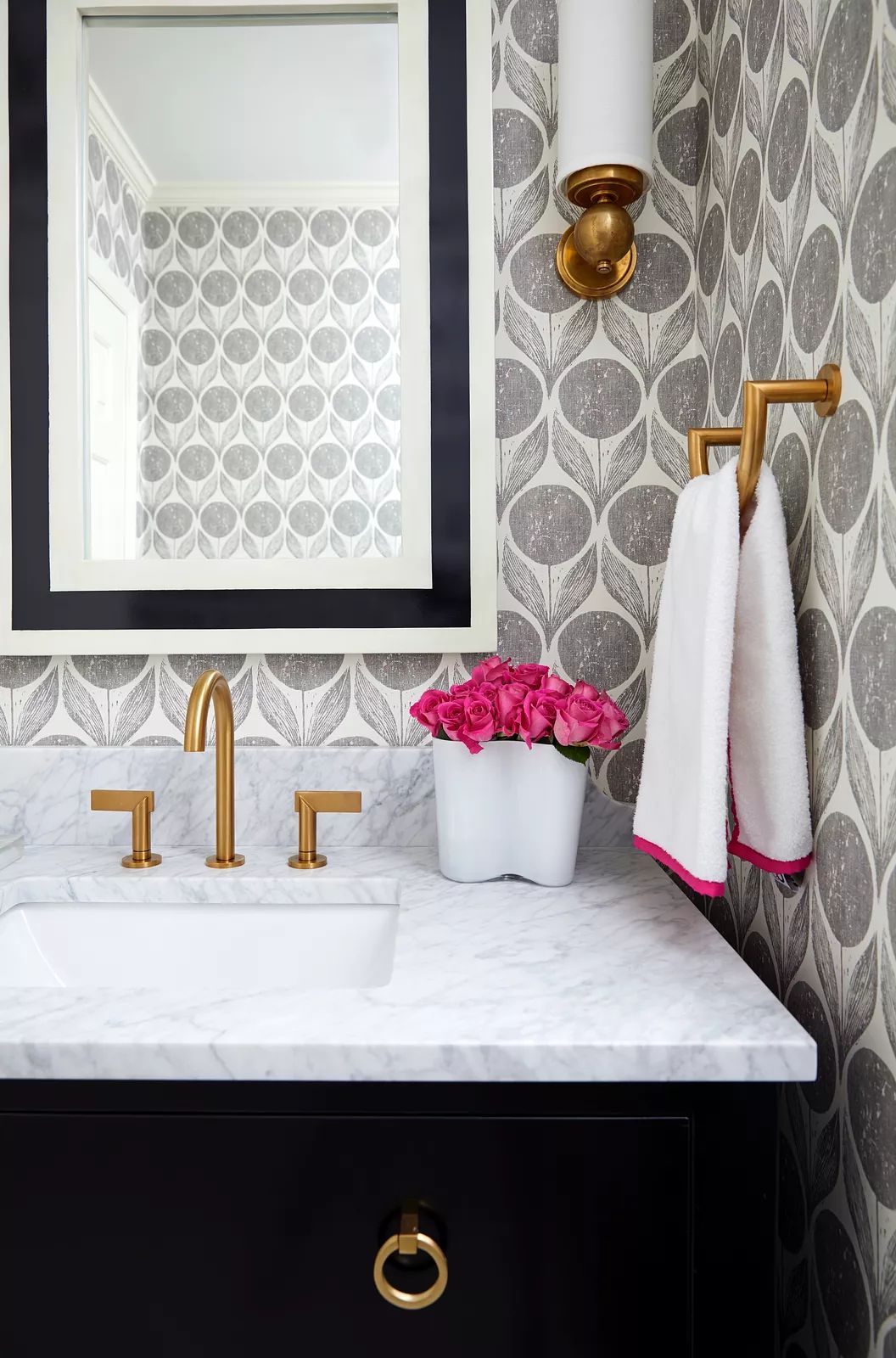 Bathroom with marble countertop, brass faucet, geometric wallpaper, and pink roses in a white container