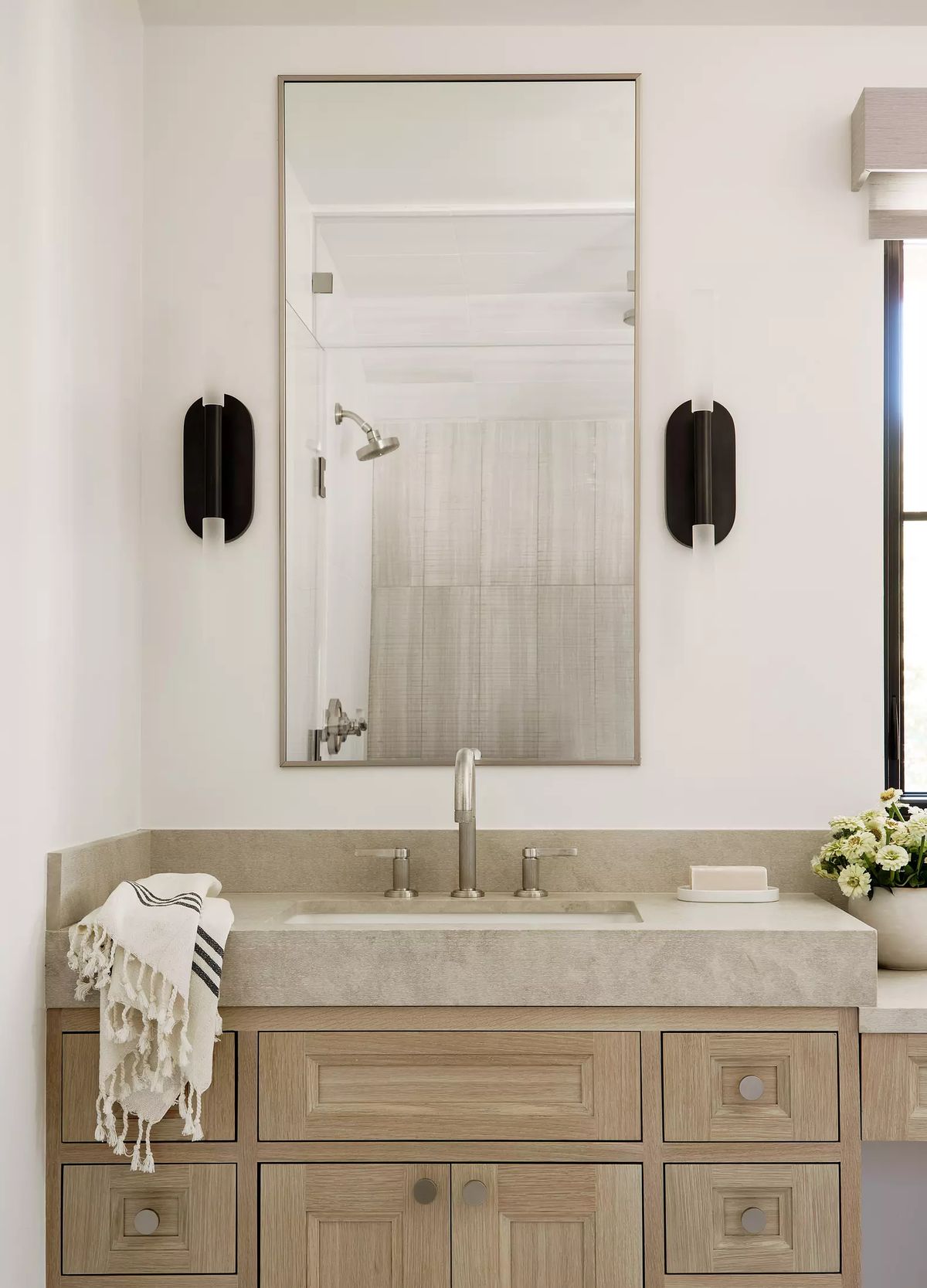 Bathroom with dual sink vanity, large mirror, black sconces, and flowers on the countertop
