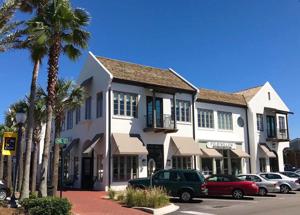Exterior front of a two-story building with gabled roof, large windows, balcony, and palm trees.