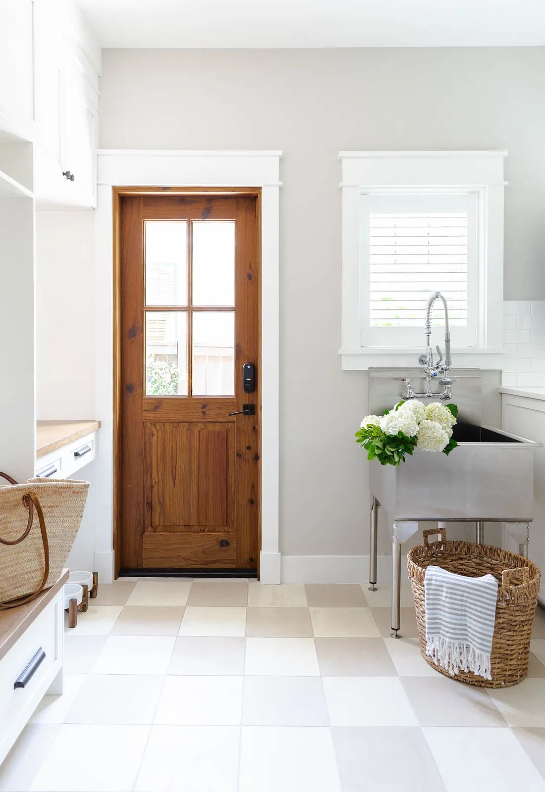 Laundry room with wooden door, stainless steel sink, checkered tiles, and wall-mounted shelf