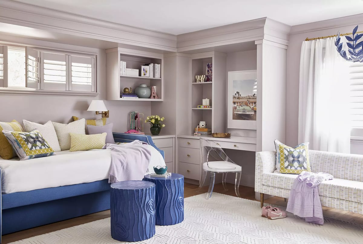 Bedroom with blue bed frame, decorative pillows, built-in shelving, desk, chair, and woven bench