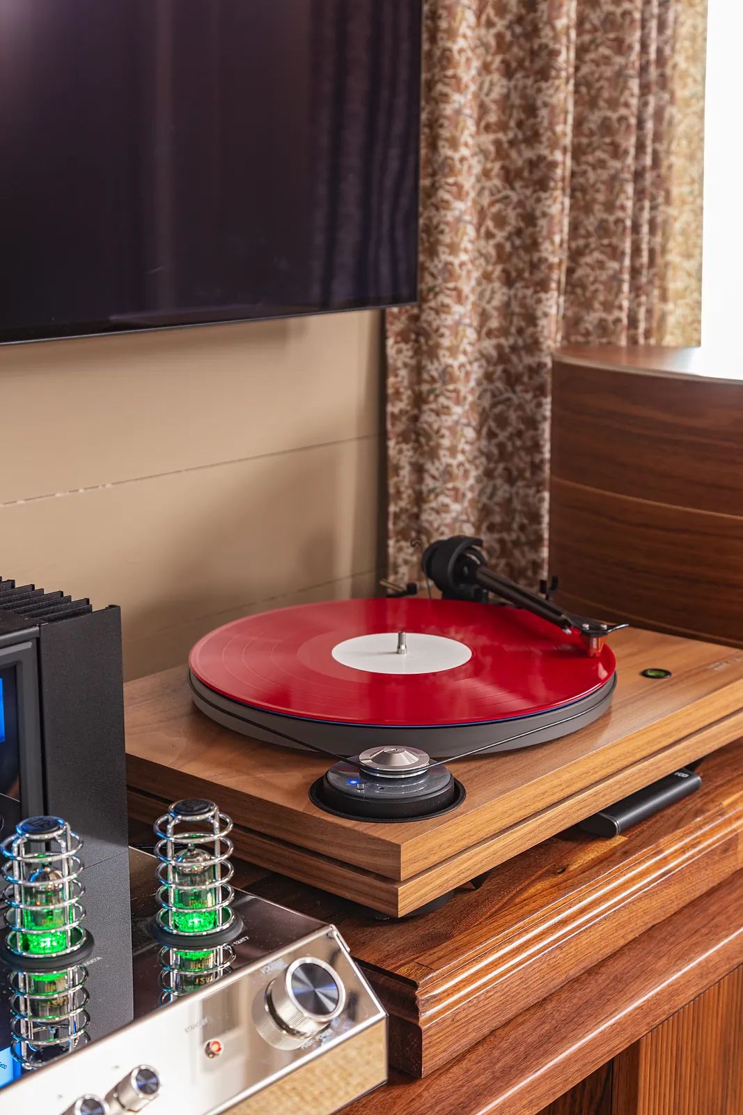Audio setup with red turntable, wood console, audio equipment, and floral patterned curtain.