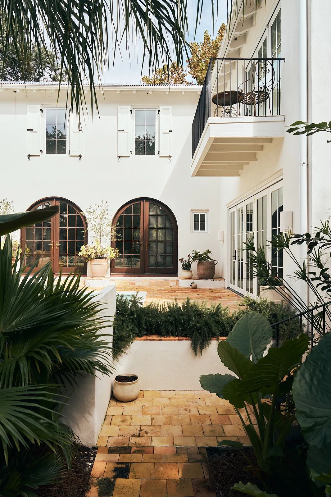 Exterior rear space with terracotta pathway, arched windows, balcony, and surrounding greenery.