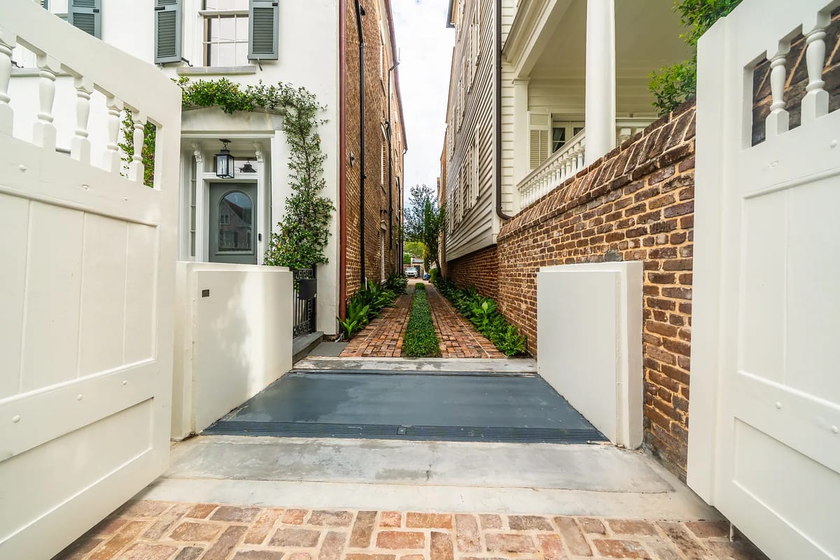 Front exterior with gated entry, brick path, and greenery between two buildings.