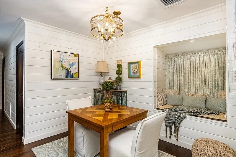 Dining room with wooden parquet table, upholstered chairs, built-in bench, lamp, and shiplap walls.