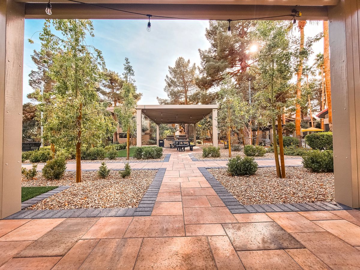 Garden with stone pathway, gazebo, table, shrubs, and trees.