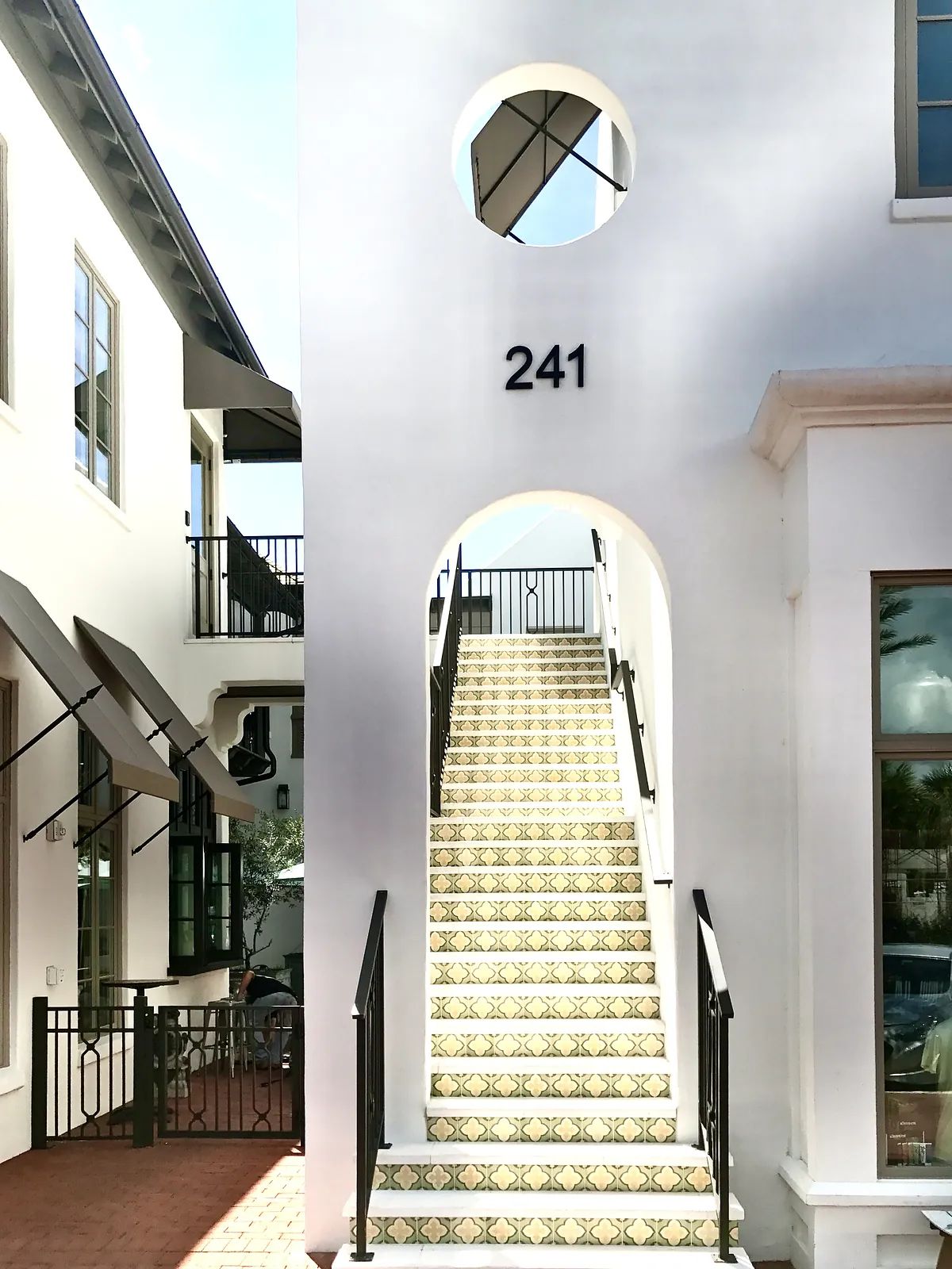 Exterior front with white building, arched entrance, patterned stairs, and number '241'.