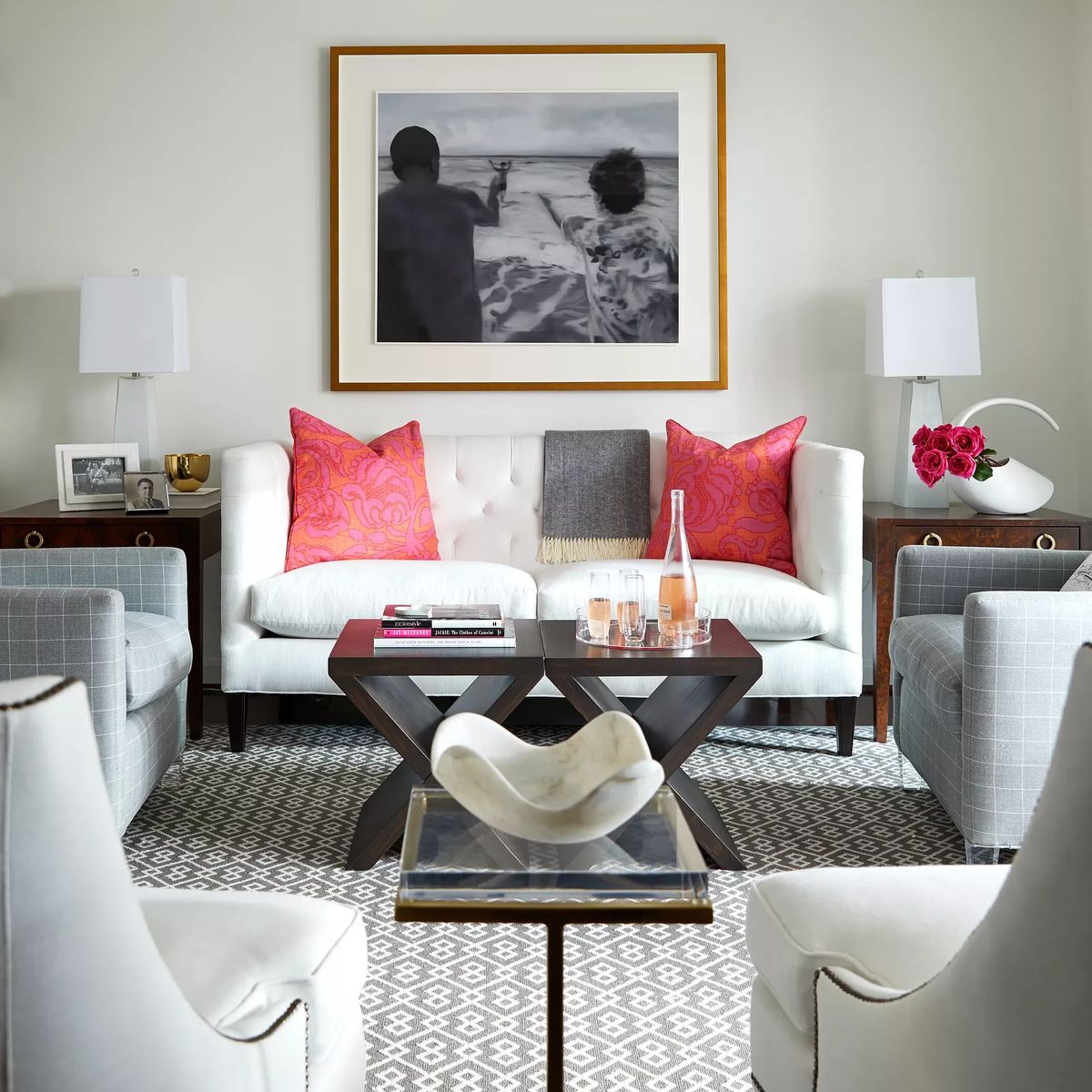 Living room with white tufted sofa, gray chairs, dark wood coffee table, lamps, and large framed photograph