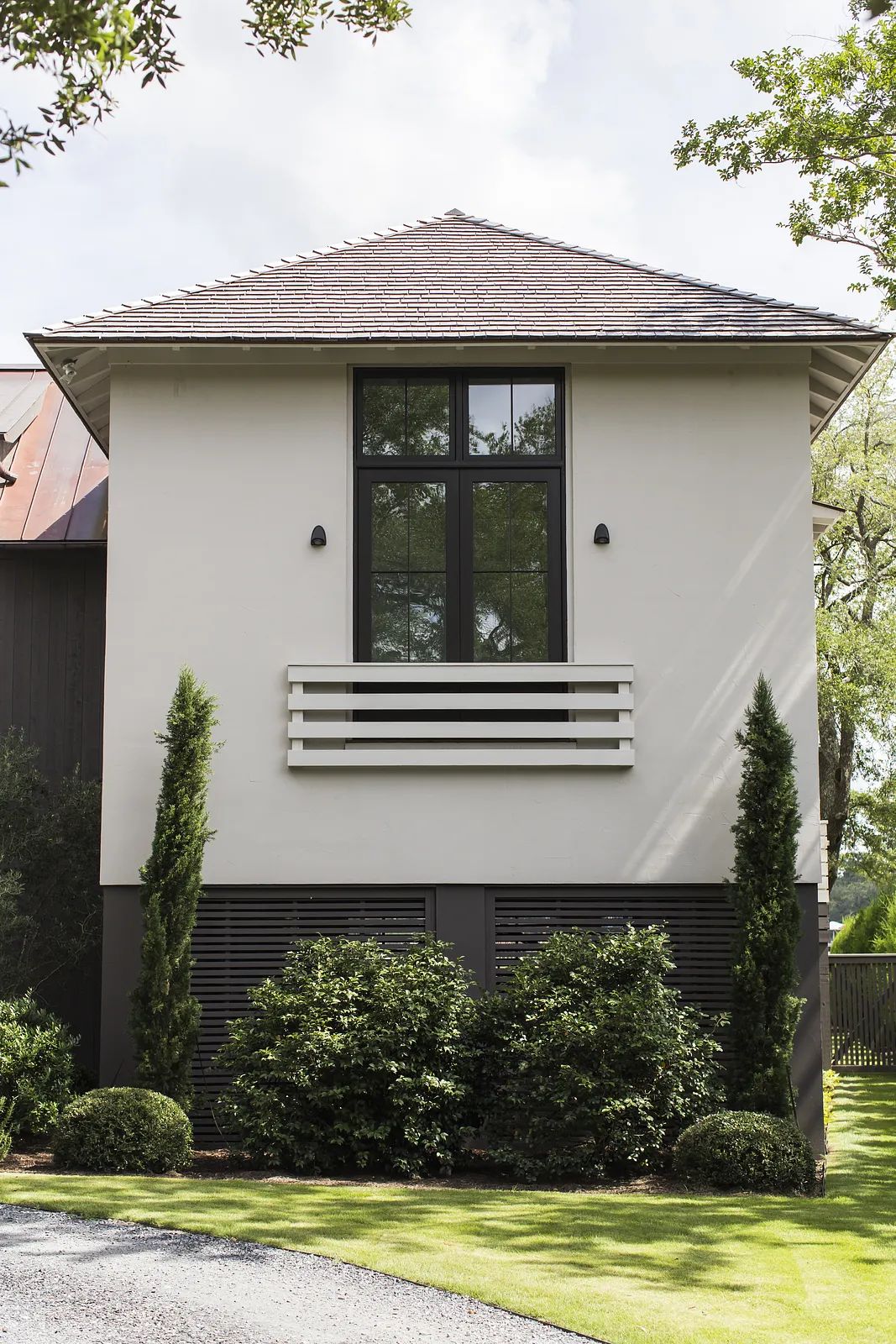 Exterior view of a house with sloped roof, large window, balcony, and landscaped shrubs.