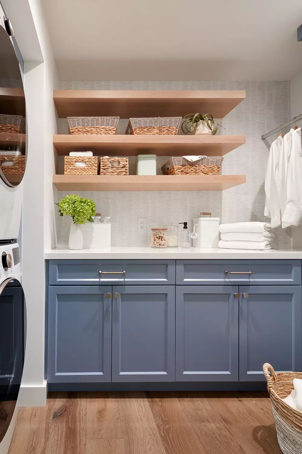 Laundry room with stacked washer, blue cabinetry, countertop, open shelving, and woven baskets.
