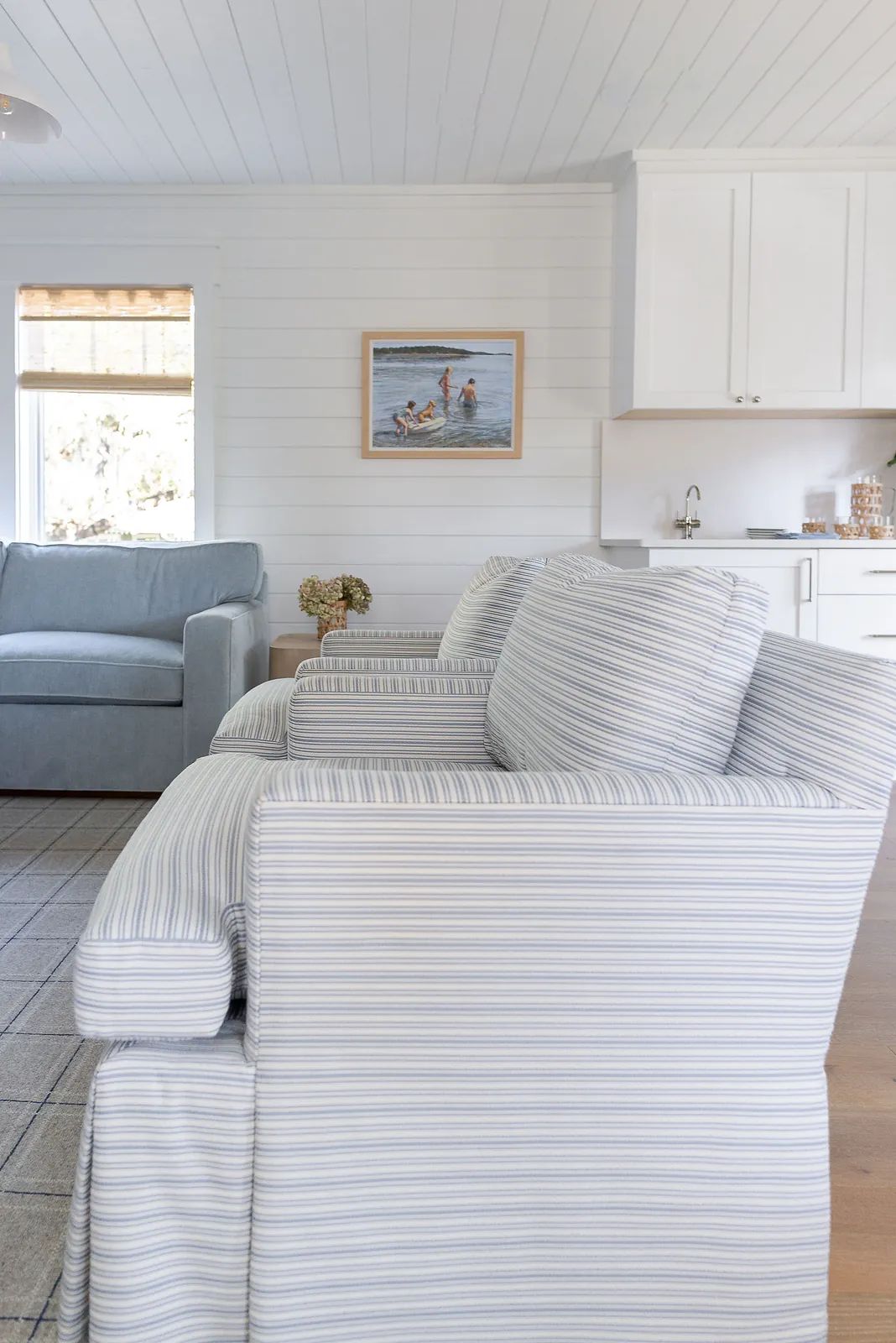 Living room with striped chairs, blue sofa, framed painting, window, and wood flooring.