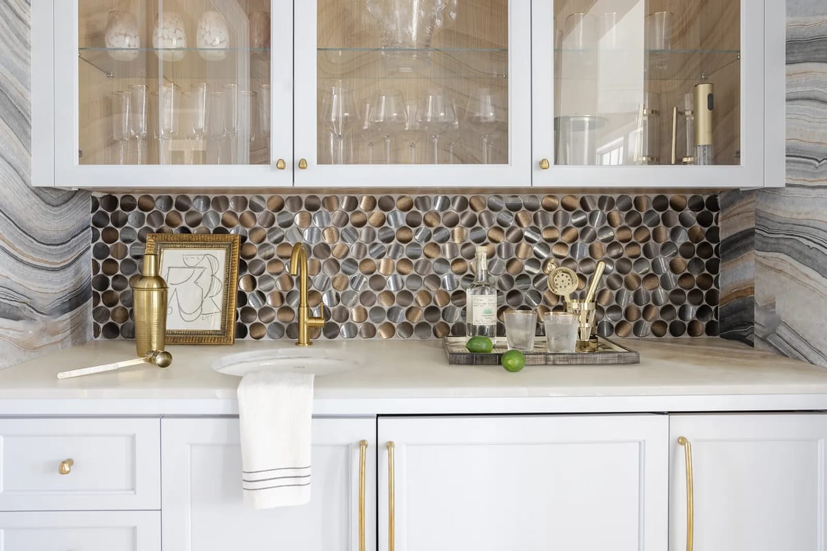 Kitchen countertop with white cabinets, sink, pebble stone backsplash, and kitchen accessories on a tray.