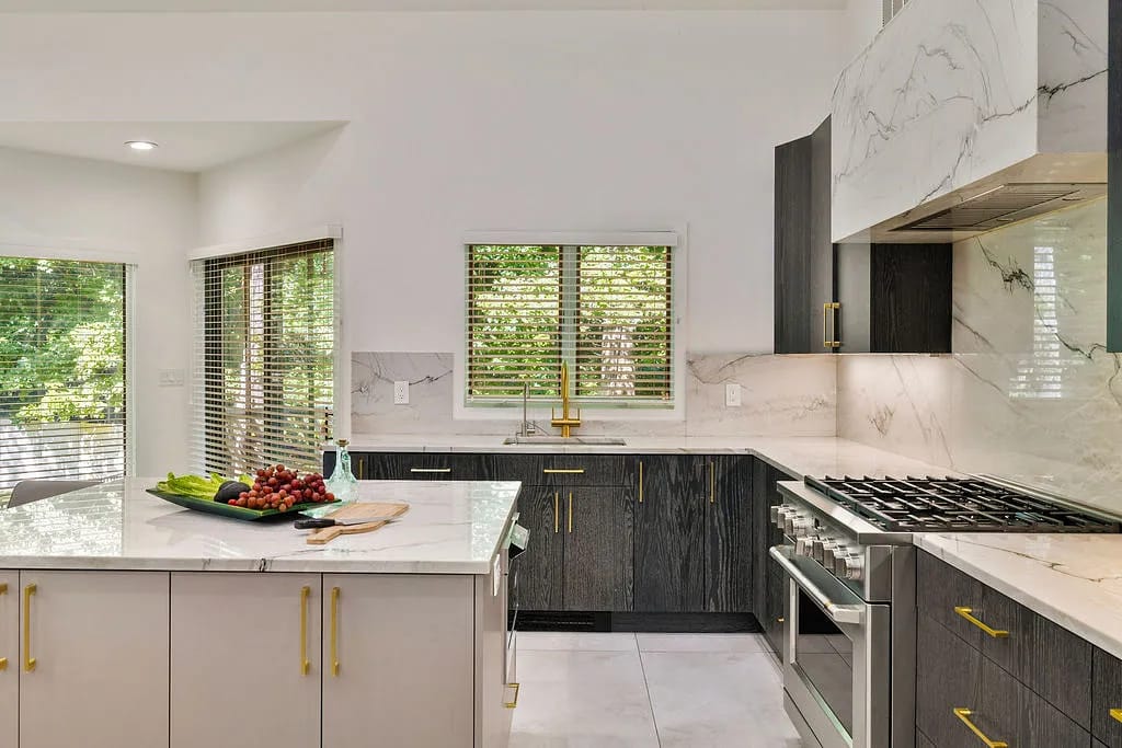 Kitchen with island, white countertop, dark cabinetry, stainless steel oven, and marble backsplash with natural light