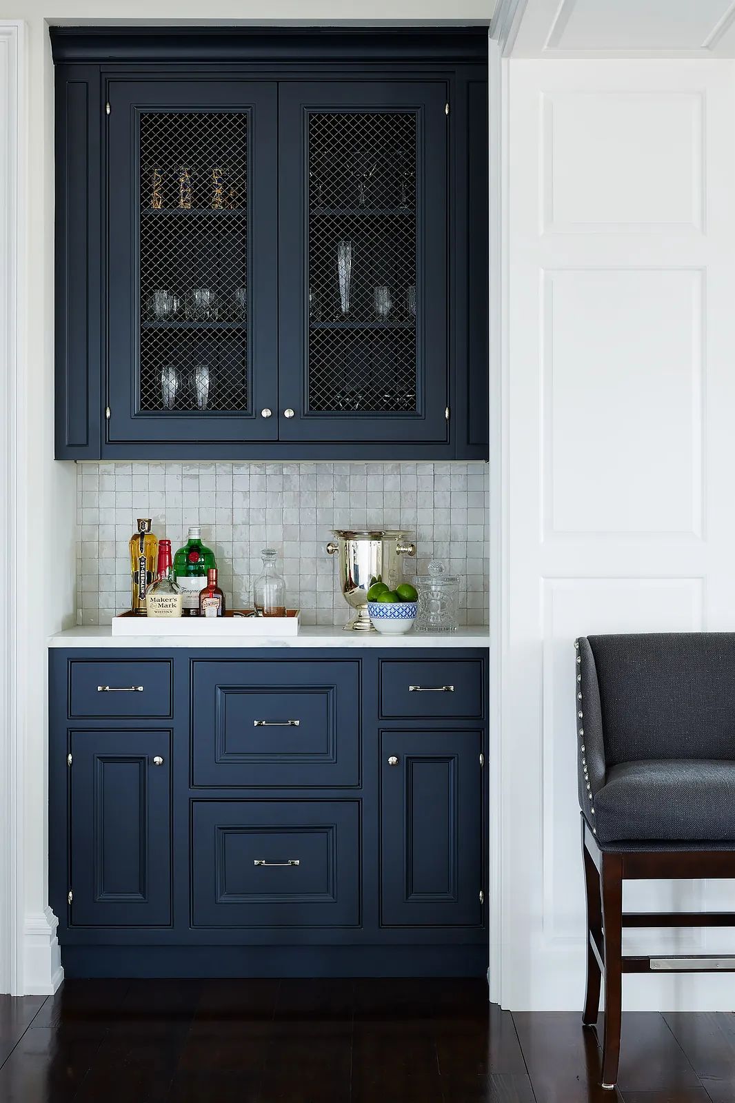 Butler's pantry with dark blue cabinetry, white countertops, sink, tiled backsplash, and bar stool.