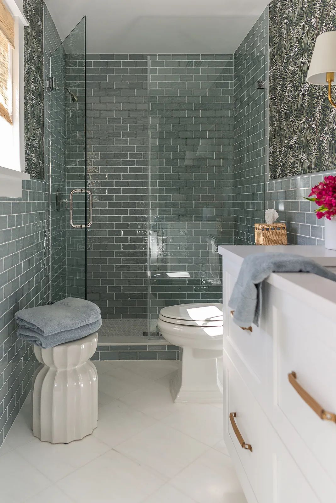 Bathroom with gray glass tile walls, white vanity, glass shower, and floral wallpaper