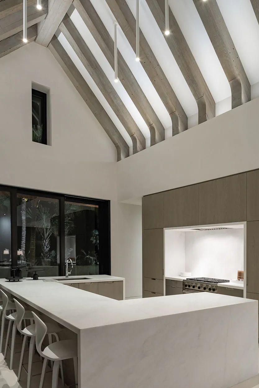 Kitchen with white marble island, beige cabinetry, stainless steel stove, and wooden beam ceiling.