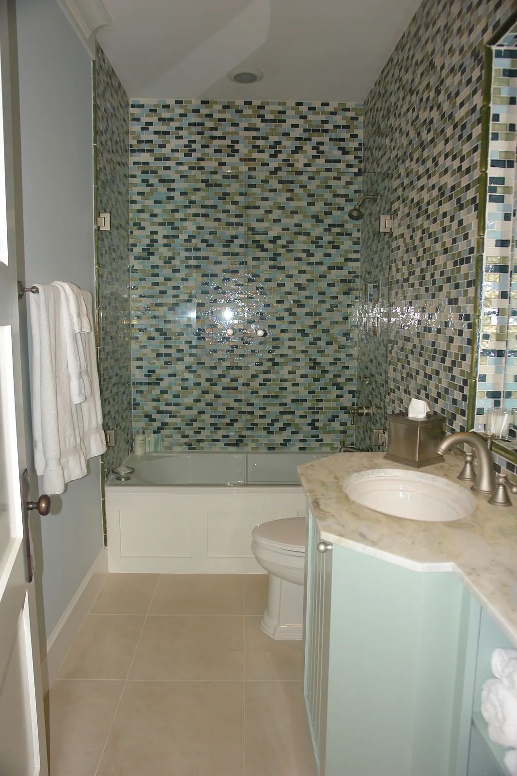 Bathroom with bathtub, tiled backsplash, marble vanity, and light-colored tiles.