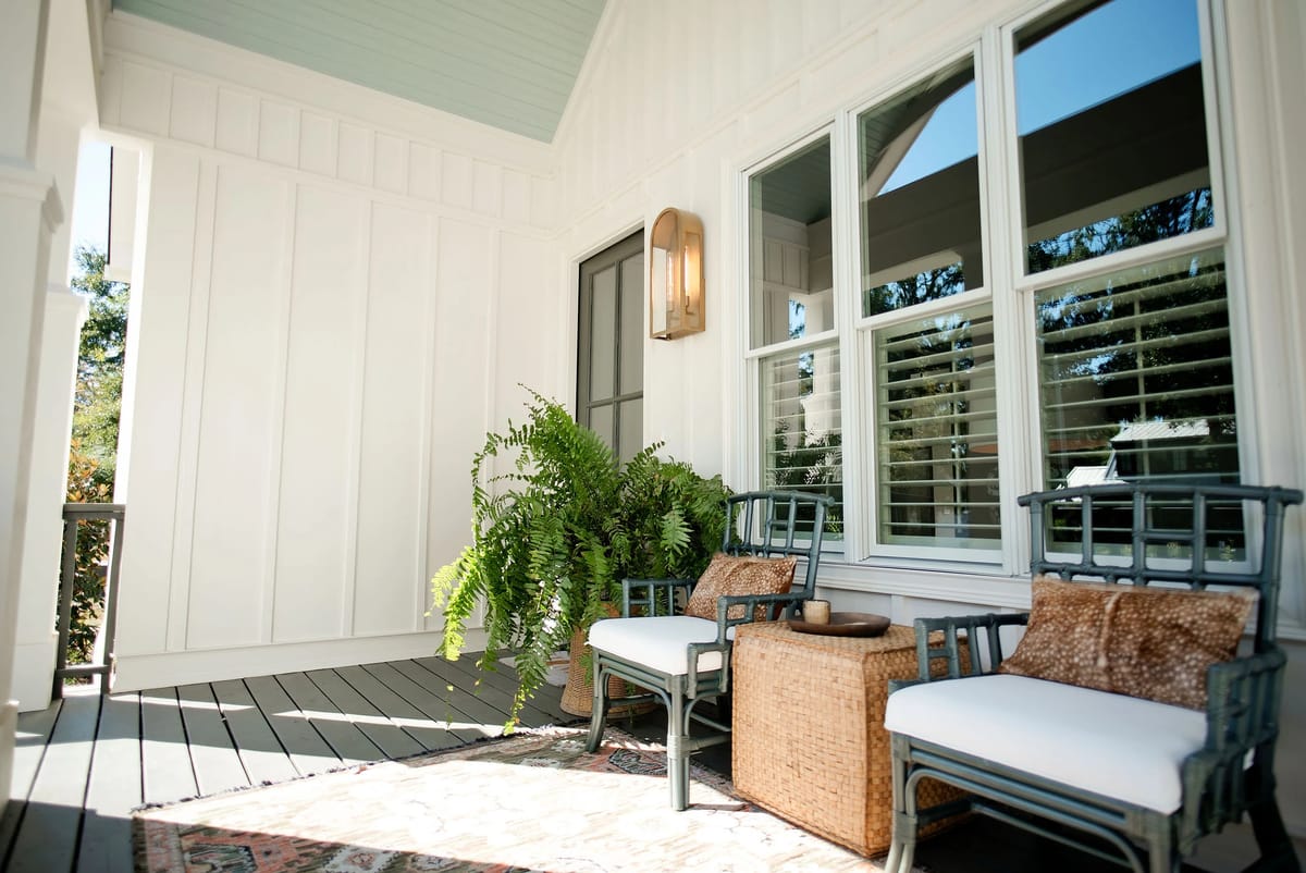 Deck with two chairs, small table, fern plant, and patterned rug on wooden flooring.