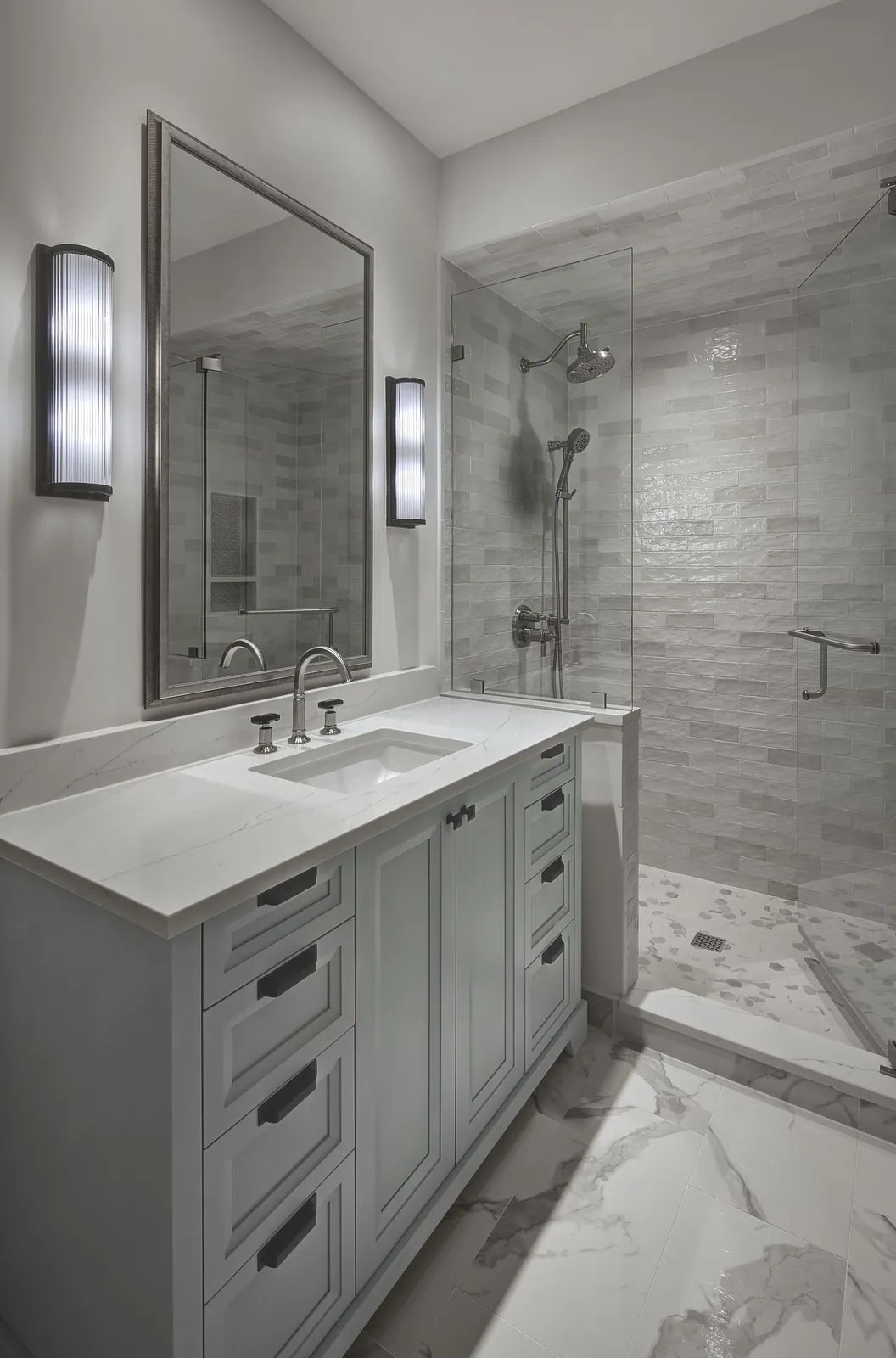 Bathroom with gray vanity, white countertop, glass shower, large mirror, and wall sconces.