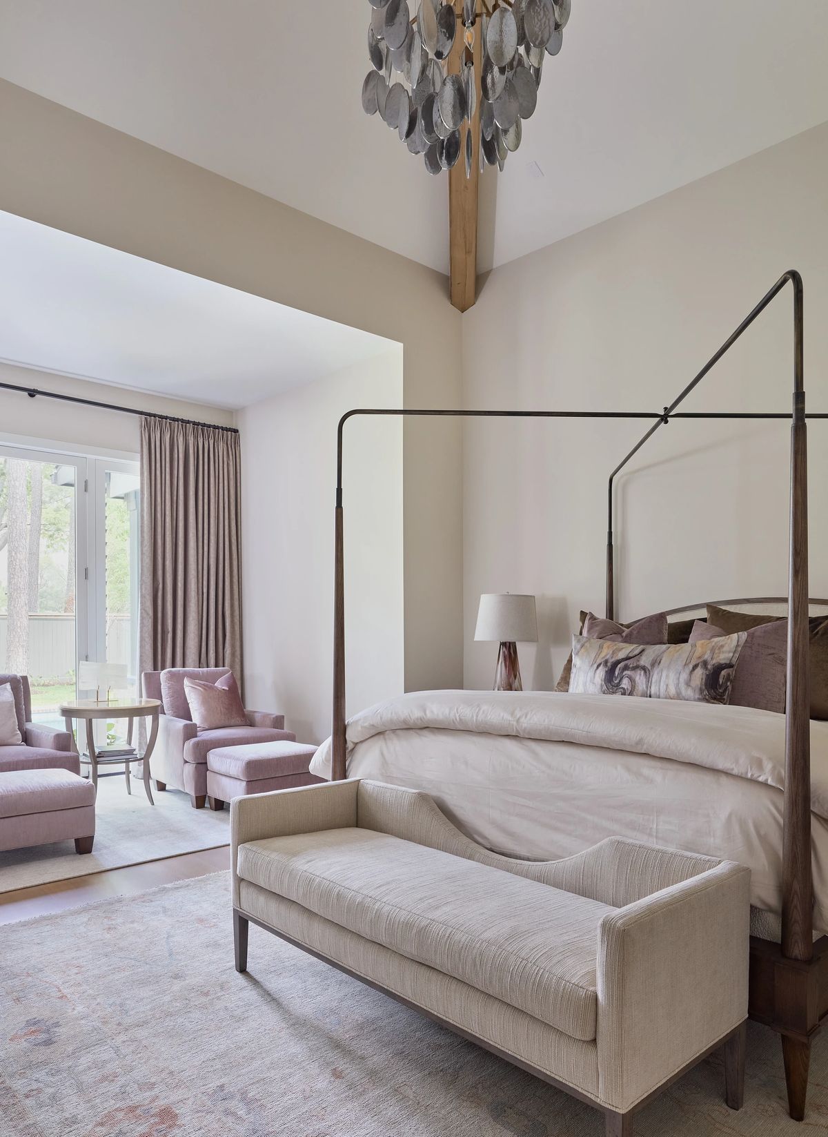 Bedroom with canopy bed, bench, chairs, round table, and wooden beams in a beige setting.