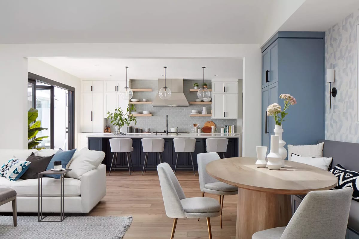 Kitchen with island, bar stools, white and navy cabinets, and adjacent dining area with round table and chairs.