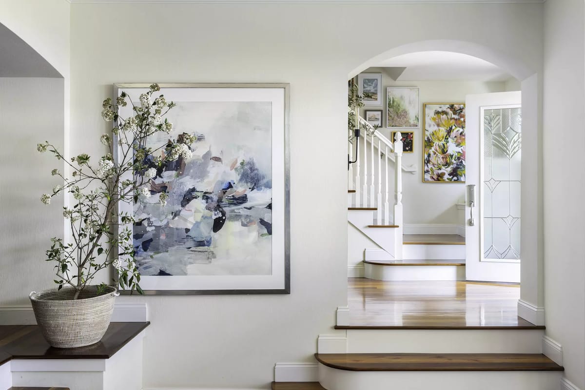 Foyer with staircase, wall art, potted plant, and door with glass panels.