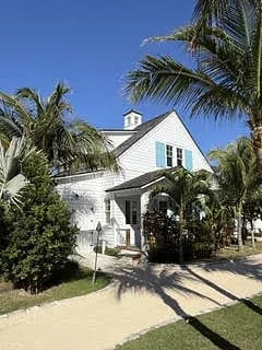 Exterior front of a house with white siding, blue shutters, palm trees, and a sandy path.