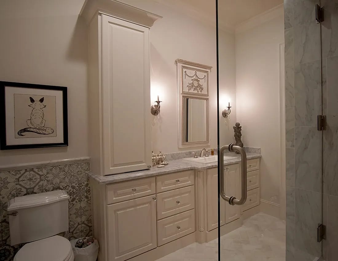 Bathroom with white vanity, marble countertop, framed mirror, wall sconces, and decorative tile.